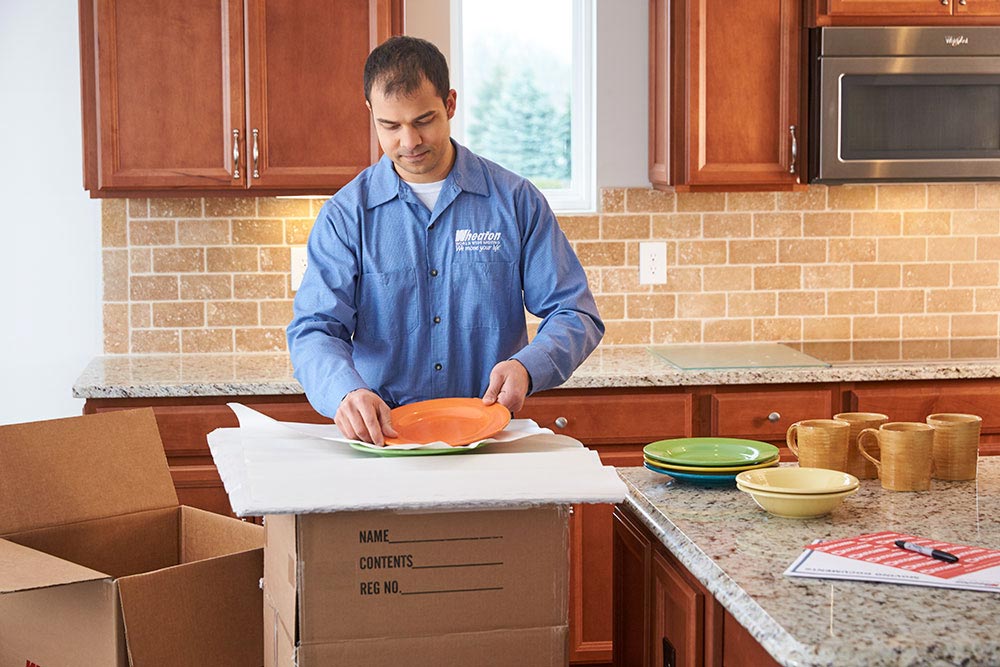 A mover from Wheaton Worldwide Moving packing up some dishes in a kitchen