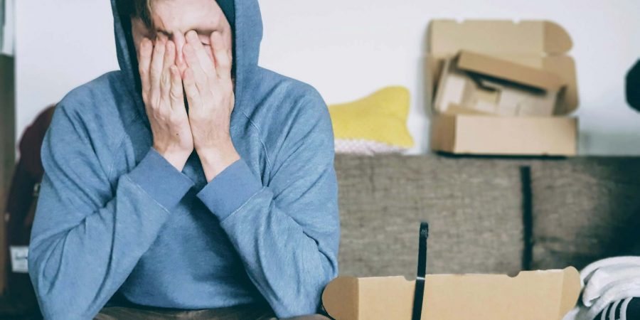 Visibly stressed man with head in his hands, on couch surrounded by boxes